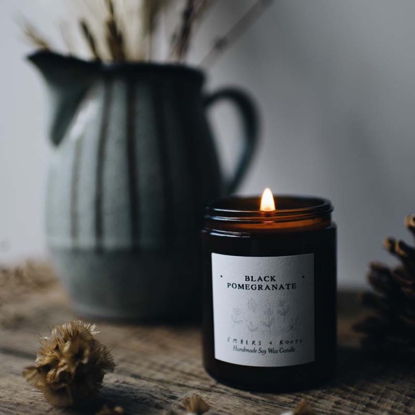 Black Pomegranate soy candle, lit, on a weathered wooden surface