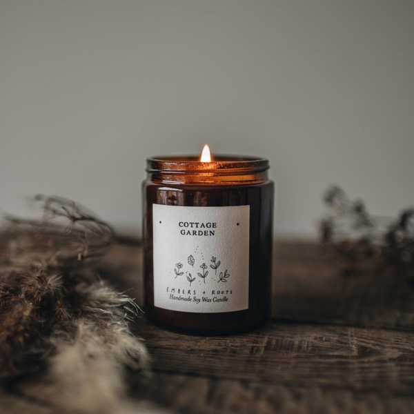 Cottage Garden soy candle, lit, on a weathered wooden surface