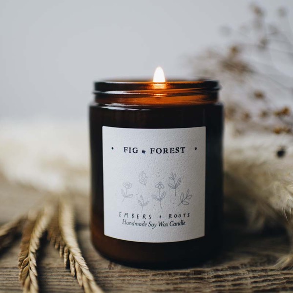 Fig & Forest soy candle, lit, on a weathered wooden surface