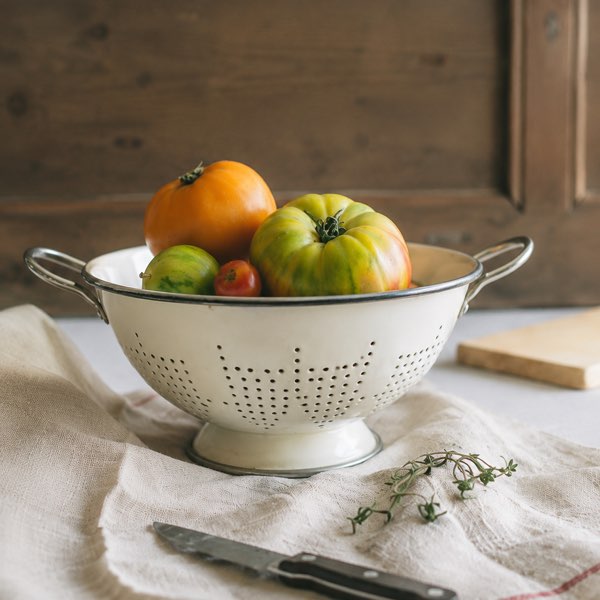 An enamel colander of just-picked heirloom tomatoes on a linen cloth